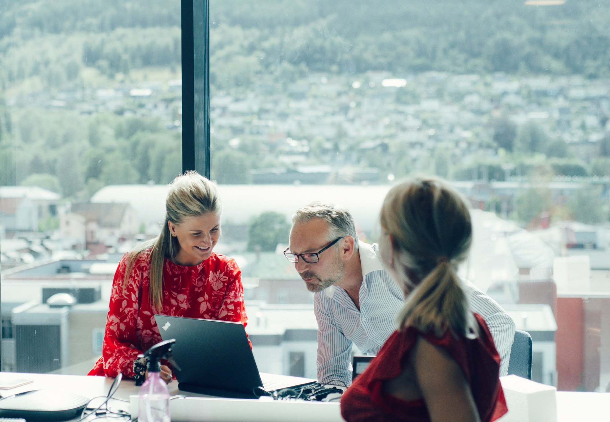 Tre kolleger sidder ved et bord, engageret med en bærbar computer, og samarbejder om et projekt.