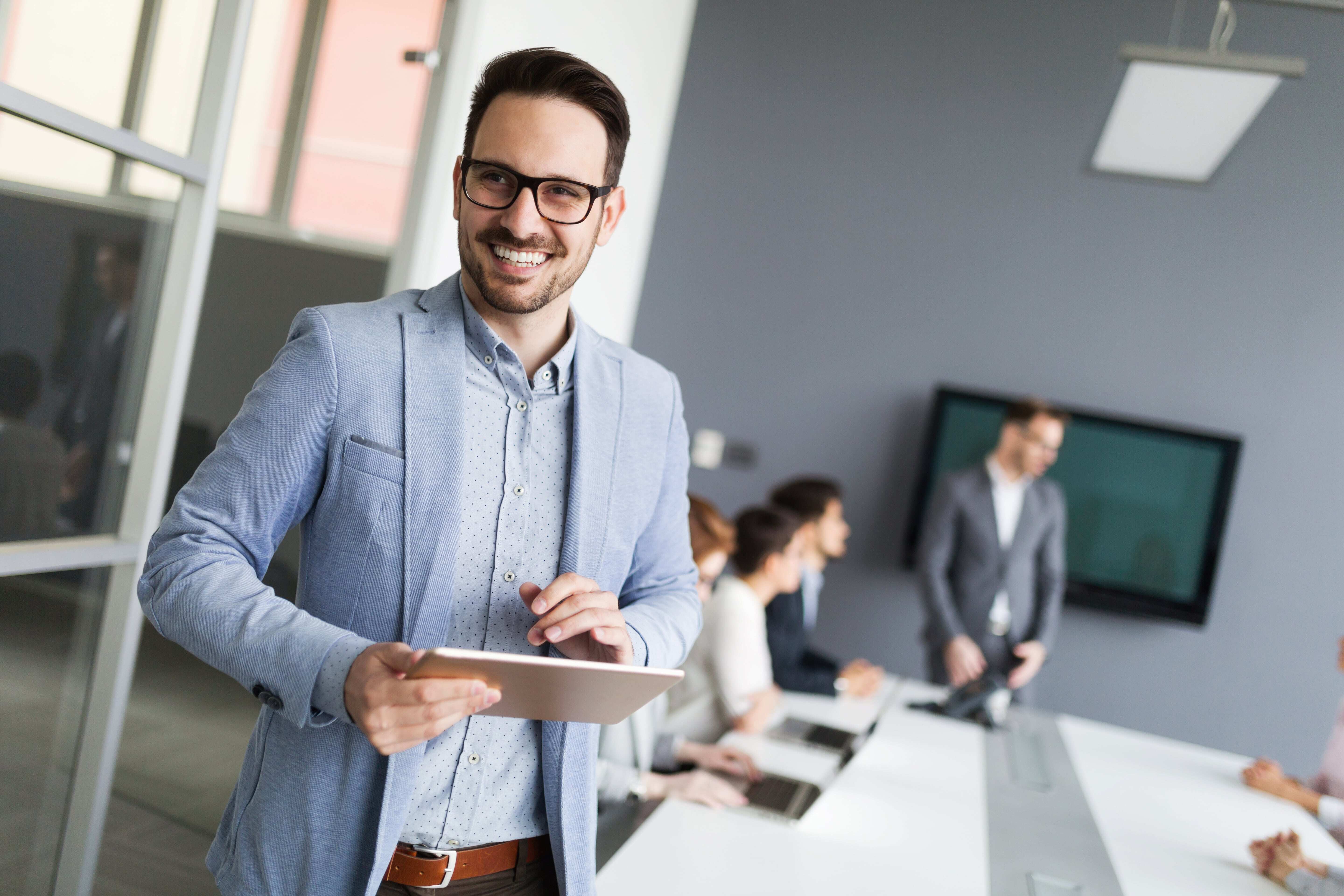 Smiling man standing in a board room with an iPad in his hand. 